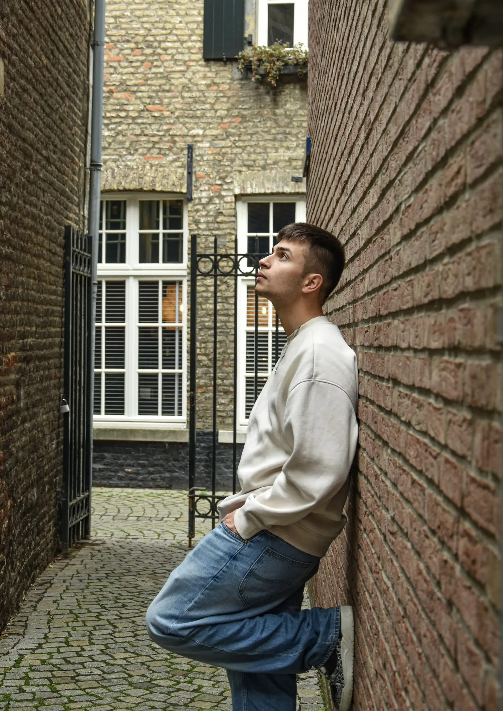 Rafael leunt in een smalle steeg tegen een bakstenen muur en kijkt omhoog