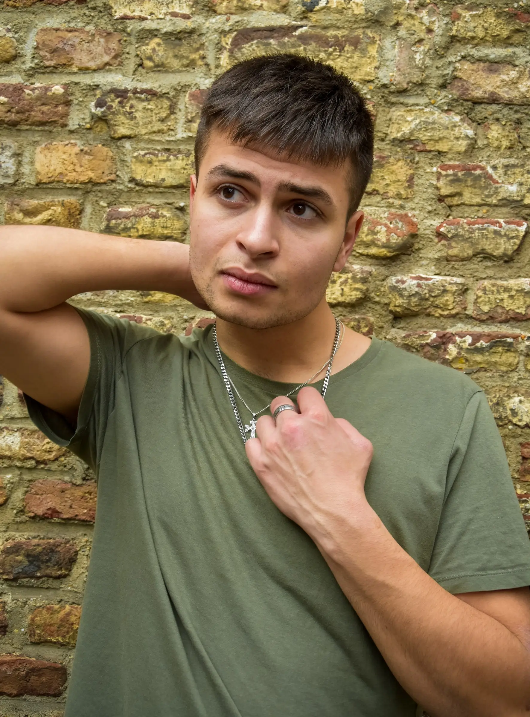 Rafael in groen shirt voor een bakstenen muur, hand bij zijn nek